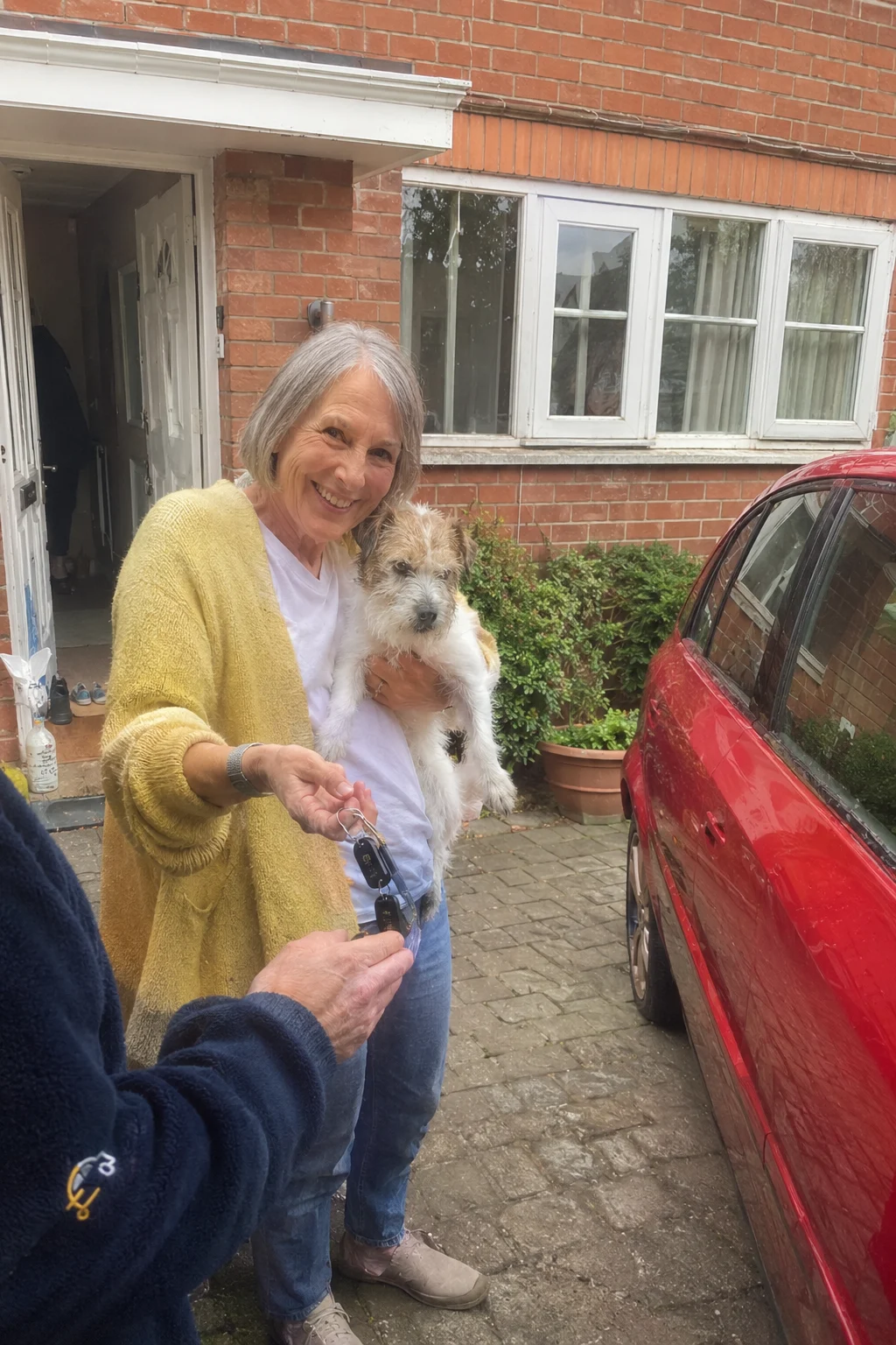A woman on her doorstep holding her terrier and handing her car keys to a Motormoolah driver
